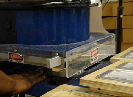 Figure 2: A close view of the opening of the heat sealer. A person’s hand will fit in the opening below the guard to the left. Two "Danger" stickers are visible.